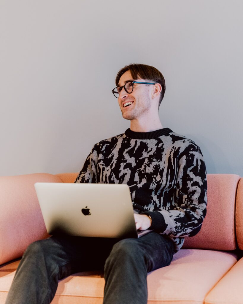 Ben sitting on a pink couch with his laptop on his lap.