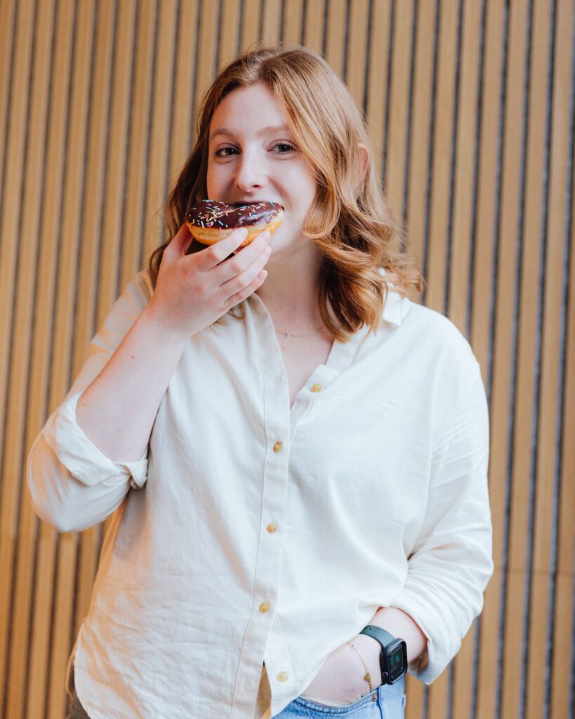 Social Media Manager AimÃ©e eating a chocolate sprinkles donut.